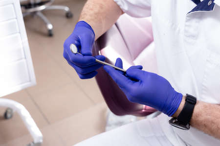 Dental mirror in male hands with blue medical glovesの写真素材