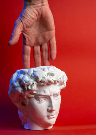 Plaster pot in the form of Davids head and male hand on a red background.の写真素材