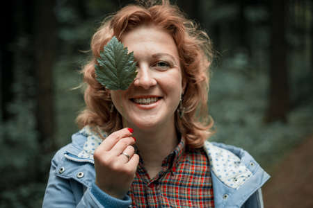 The blonde woman covers her eyes with green leaves.