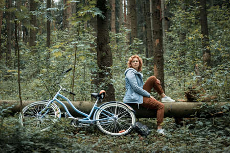 Woman with blue bike sitting on a fallen tree in the forestの写真素材
