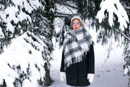 A blonde woman in winter stands under a fir-tree in the snow.の写真素材
