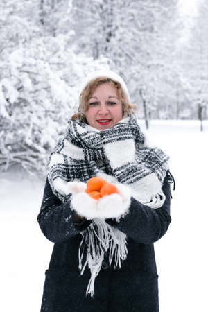 Woman blonde in winter with tangerines in handsの写真素材