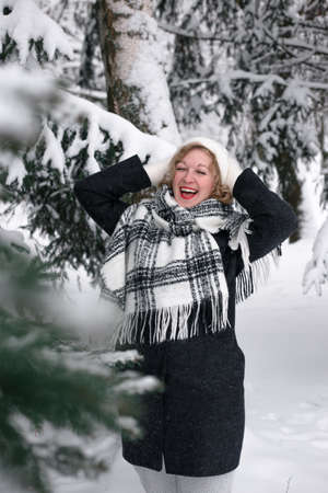 A blonde woman in winter stands under a fir-tree in the snow.の写真素材