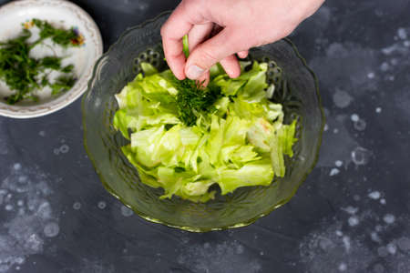 Adding greens to salad in a glass plate on a gray tableの写真素材