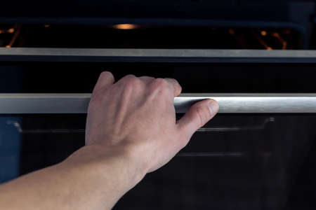 The hand opens the oven door. Kitchen equipment.