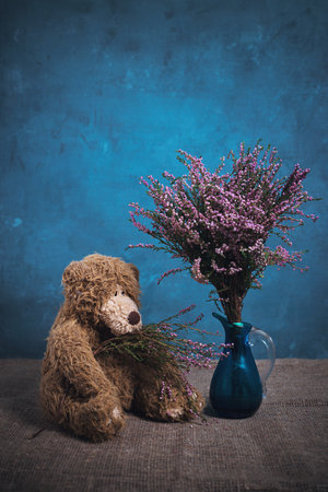 Still life with a teddy bear and heather in a vase on a blue backgroundの写真素材