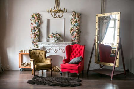 bright loft-style room with a red armchair, a brown armchair, a white fireplace with flowers, a...