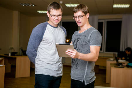 Two young people are discussing a project in the office. Standing next to each other, one of them...