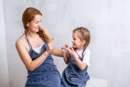 Repair in the apartment. Happy family mother and daughter in aprons paint the wall with white paint. Mother and daughter smeared each other with paint and laughの写真素材