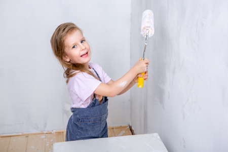 Repair in the apartment. Happy family mother and daughter in aprons paint the wall with white paint. girl holding paint roller in hand and laughingの写真素材