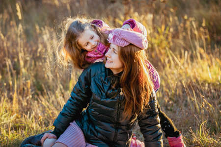 Young beautiful mother with her daughter on a walk on a sunny autumn day. Daughter is trying to put...