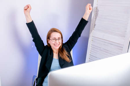 Portrait of happy young successful businesswoman celebrate something with arms up at office. Positive emotion. Big deal, promotion, lottery win or discount concept. Black Friday or Cyber Monday.の写真素材