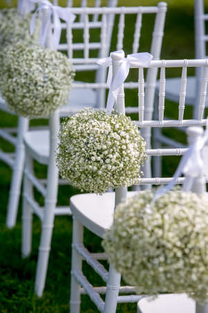 Summer outdoor wedding ceremony decoration. White chairs decorated with gypsophila balls, vertical view.の写真素材