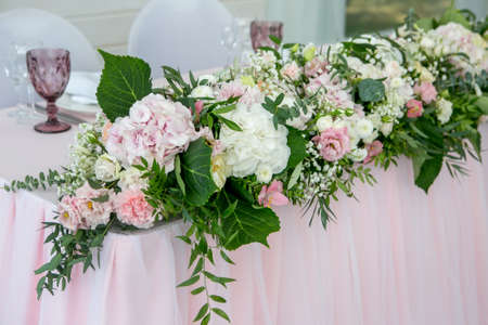Beautiful white dinner table for newlyweds decorated with greenery and long cloth. Long flower arrangement of hydrangeas, roses, gipsophiles, lilies and greenery on a white background.の写真素材