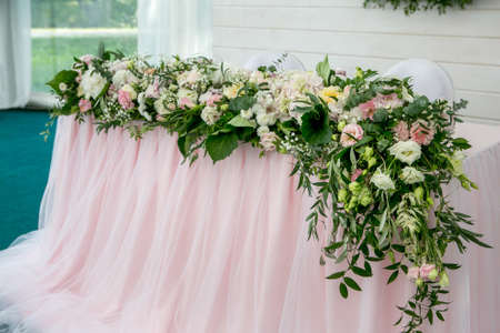 Beautiful white dinner table for newlyweds decorated with greenery and long cloth. Long flower arrangement of hydrangeas, roses, gipsophiles, lilies and greenery on a white background.の写真素材