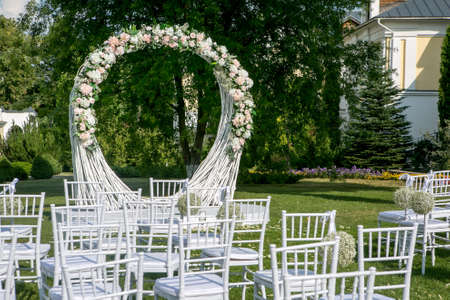 Summer outdoor wedding ceremony decoration. Beautiful white arch of branches and bouquet of white roses, hydrangeas and gypsophila on a white podium, horizontal view.の写真素材