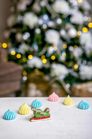 Gingerbread sleigh and meringue on the table in front of defocused lights of Christmas decorated fir...