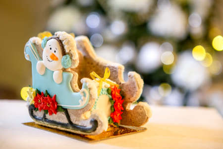 Gingerbread sleigh with snowman in front of defocused lights of Christmas decorated fir tree....