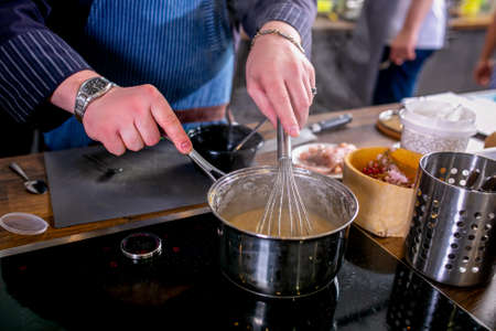The chef mixes the sauce in a saucepan using the whisk. Master class in the kitchen. The process of cooking. Step by step. Tutorial. Close-upの写真素材