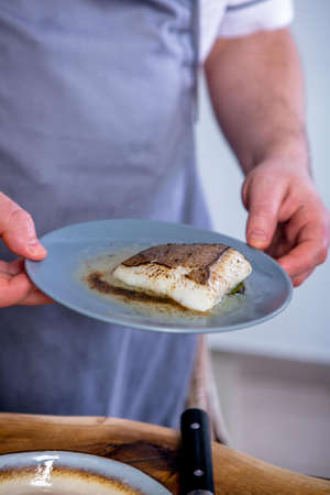 Cook holds a plate of stewed halibut. Master class in the kitchen. The process of cooking. Step by...