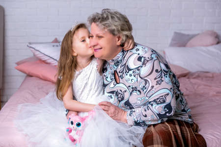 Happy little girl and her grandmother have breakfast together in a white kitchen. They are having fun and playing with fruits. Maternal care and love. Healthy eating.の写真素材