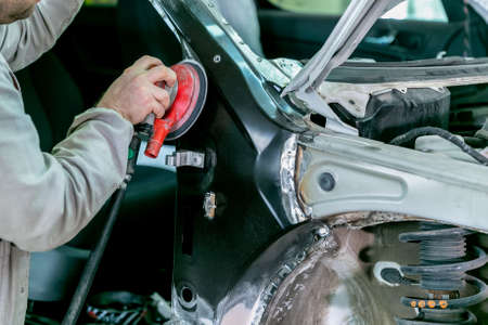 Car repair in car service. Mechanic worker repairman sanding polishing car body and preparing...