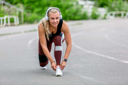 Fitness lifestyle. Young woman in headphones tying the laces before jogging. Workout at the stadium....