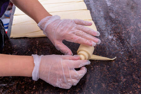 A pastry chef in the kitchen is making pastries. Chef rolls the cut dough into a croissant. Master class in the kitchen. The process of cooking. Step by step. Tutorial. Close-up.の写真素材