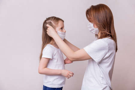 Concept of coronavirus quarantine. Mom puts on her daughter a medical mask that protects against viruses. Theme of health and medicine.の写真素材