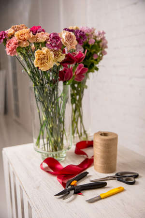 Florist's workplace. Tools and flowers before starting work on the table. Floristic's knife, scissors, pruning shear, tape, twine. Tutorial. Step by step. High quality photoの写真素材
