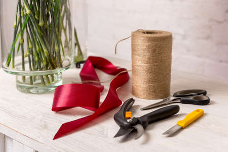 Florist's workplace. Tools and flowers before starting work on the table. Floristic's knife, scissors, pruning shear, tape, twine. Side view. Tutorial. Step by step. High quality photoの写真素材