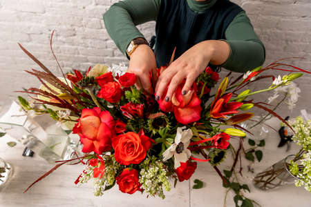Florist workplace on the background of a white brick wall. The florist composes a bouquet of orchids, roses, sunflowers, lilies, alstemeria and ornithogalum, adding flowers to it step by step. Manual.の写真素材