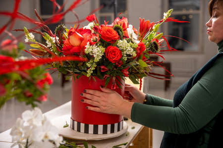Florist workplace on the background of a white brick wall. A florist examines a floral arrangement of orchids, roses, sunflowers, lilies, alstroemerias and ornithogalums in a red box. Tutorial.の写真素材