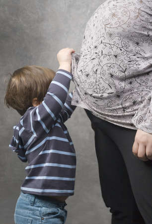 Little boy peeping under his pregnant mother's blouseの写真素材