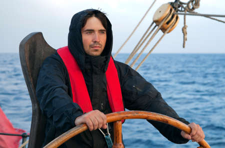 Young sailor on a ship's deck behind a steering wheelの写真素材
