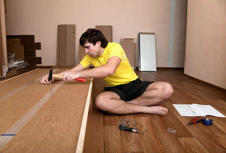 Young man sitting on floor assembling flatpack closetの写真素材