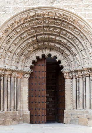 A beautifully carved stone archway frames the large wooden doors of an ancient church in Obanos, showcasing intricate craftsmanship.の写真素材