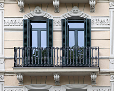 Two symmetrical balconies with wooden shutters adorn a vintage facade.の写真素材