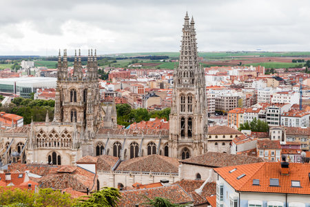 Burgos Cathedral rises majestically above the rooftops of the city, surrounded by lush greenery and buildings under gray skies.の写真素材