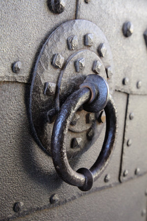 A close-up of a decorative iron door knocker on a weathered door in an old urban setting.の写真素材