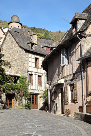 Charming street in Conques featuring quaint stone buildings and sunshine illuminating the historic...