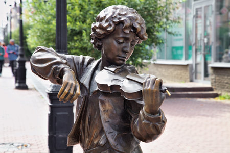 Nizhny Novgorod, Russia - August 27, 2016 - A bronze sculpture of a boy playing the violin captivates passersby on a busy streetの写真素材