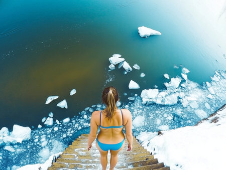 A woman in a swimsuit descends icy steps into a cold body of water surrounded by snow and ice fragments.の素材
