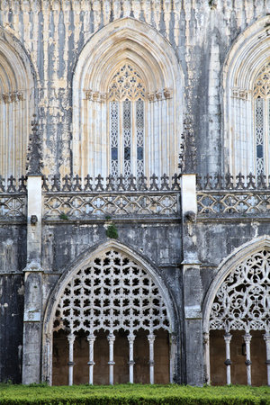 Intricate Gothic arches complement lush greenery at Batalha Monastery, showcasing historical architecture and serene landscapingの写真素材