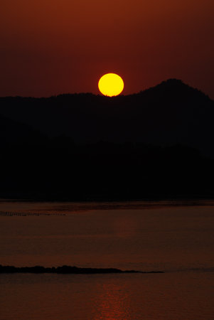Sunset over the sea with a silhouette of a mountain in the backgroundの写真素材