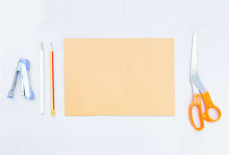 stapler pencil brown sheet paper and scissors, handcraft tools placed on gray background, leave...