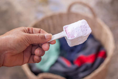 old hand hold the spoon detergent and have a basket of fabric on backgroundの写真素材