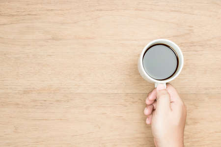 yellow brown skin tone hand holding white coffee cup wood texture , from top viewの写真素材