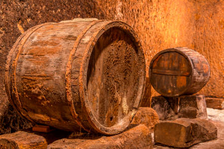 Old oak barrel with rusty hoops. Deep wine cellar with textured wallsの写真素材