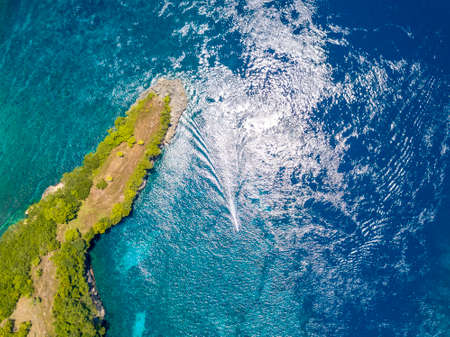 Indonesia. Emerald surface of the ocean. A small boat trimaran near a tropical island, overgrown with jungle. Aerial view vertically downの写真素材